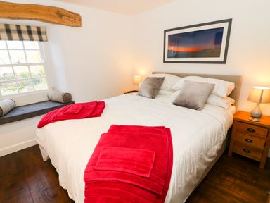 A bedroom with a bed with white bedding and red towels by a window seat with cushions at Linden Cottage in Ravenstonedale Nr Kirby Stephen
