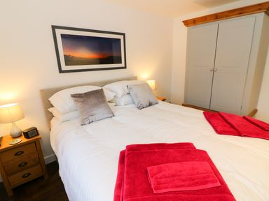 A bedroom with a double bed bedside tables lamps a wardrobe and red towels at Linden Cottage in Ravenstonedale Nr Kirby Stephen