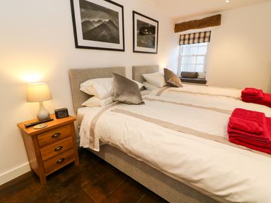 A bedroom with twin beds bedside table with lamp and remote control and a window with checked blind at Linden Cottage Ravenstonedale Nr Kirby Stephen
