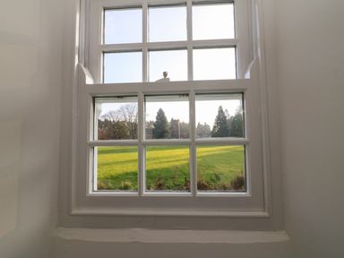 A window with white frames showing a green lawn and trees outside at Linden Cottage in Ravenstonedale Nr Kirby Stephen