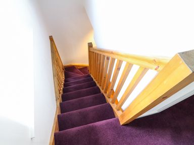 A staircase with purple carpet and wooden railing at Linden Cottage in Ravenstonedale Nr Kirby Stephen