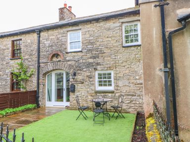 A stone cottage exterior with white framed windows and a small table with three chairs on a grass area at Linden Cottage Ravenstonedale Nr Kirby Stephen