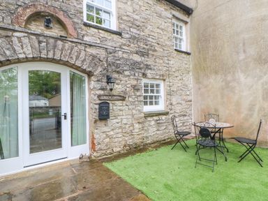 A stone cottage exterior with a white door a small window a black mailbox a wall lamp and a metal table with four chairs on artificial grass at Linden Cottage Ravenstonedale Nr Kirby Stephen