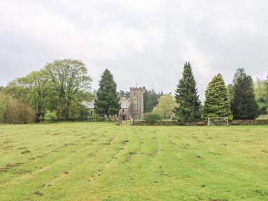 A large grassy field with two soccer goals and a stone building with a tower surrounded by trees at Linden Cottage in Ravenstonedale Nr Kirby Stephen