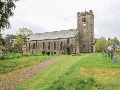 A stone church with a clock tower surrounded by gravestones and green grass at Linden Cottage in Ravenstonedale Nr Kirby Stephen