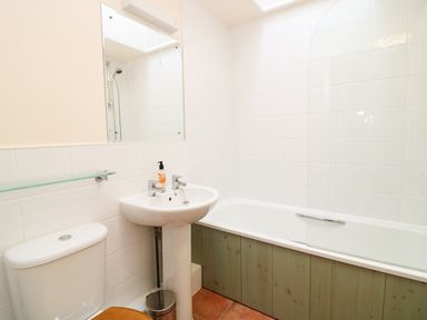 A bathroom with a toilet a pedestal sink with soap a bathtub with a partial glass screen and a mirror above the sink at Oreos Cottage in St Agnes