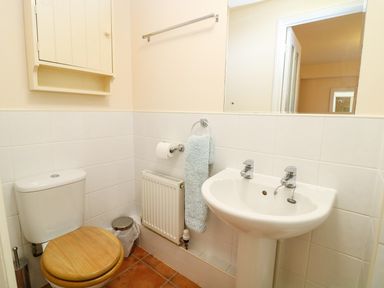 A bathroom with a toilet wooden seat white sink towel and wall cabinet at Oreos Cottage in St Agnes