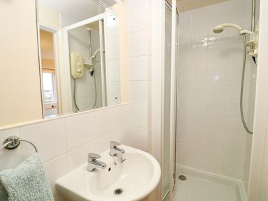 A bathroom with a white sink and two taps a shower enclosure with a showerhead and a mirror at Oreos Cottage in St Agnes
