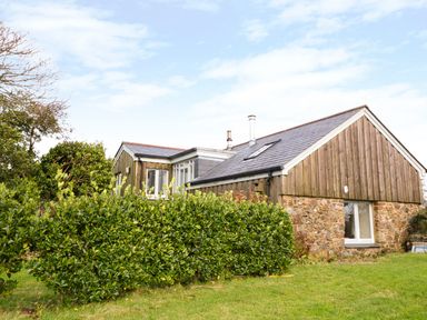 A stone and wood exterior house with a small garden and bushes in the foreground at Oreos Cottage in St Agnes