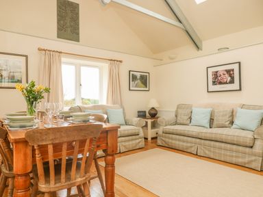 A living room with a wooden dining table set with plates and glasses and plaid sofas with cushions at Oreos Cottage in St Agnes