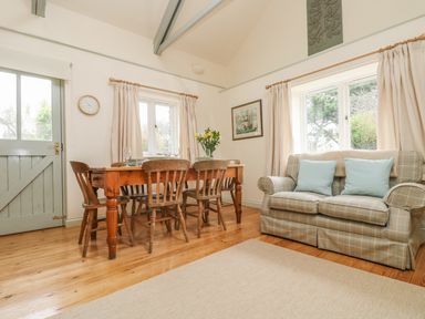 A dining area with a wooden table and chairs next to a plaid sofa with cushions at Oreo's Cottage in St Agnes