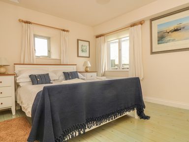A bedroom with a double bed with blue blanket and striped pillows two bedside tables with lamps two windows with curtains and paintings on walls at Oreo's Cottage in St Agnes