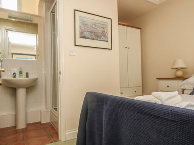A bedroom with a bed covered with a dark blanket and white towels beside a bedside table with a lamp and a wardrobe with an adjoining bathroom at Oreos Cottage in St Agnes