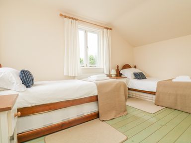 A bedroom with two single beds bedside table and window with white curtains at Oreos Cottage in St Agnes