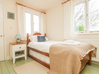 A bedroom with a single wooden bed a bedside table with a lamp and windows with white curtains at Oreos Cottage in St Agnes