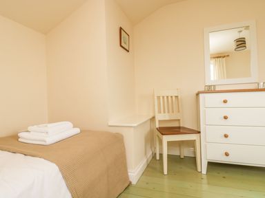 A bedroom with a bed covered by a blanket with folded towels on top a chair next to a white chest of drawers with a mirror on the wall at Oreos Cottage in St Agnes