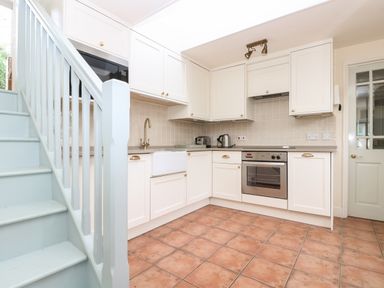 A kitchen with white cabinets a stove microwave kettle and toaster next to light blue stairs at Oreos Cottage in St Agnes