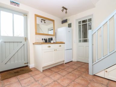A kitchen area with a wooden countertop cabinet coffee machine white refrigerator tiled floor and stairs at Oreos Cottage in St Agnes