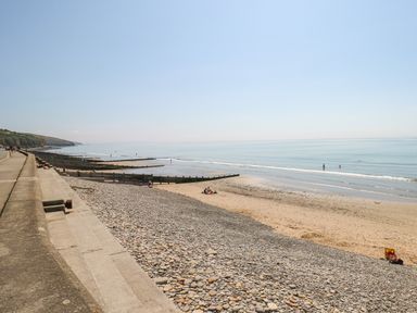 A beach with pebbles and sand next to a seawall with steps at The Lodge in Rosemarket