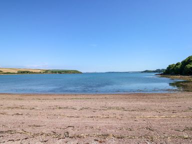 A beach with pebbles and seaweed leading to calm water with land and trees at The Lodge in Rosemarket