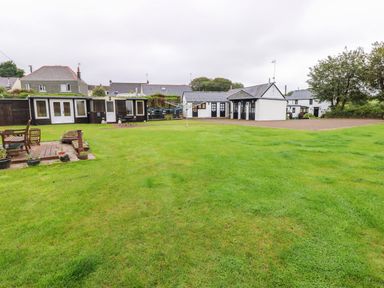 A large grassy yard with outdoor furniture and multiple buildings in the background at The Lodge in Rosemarket