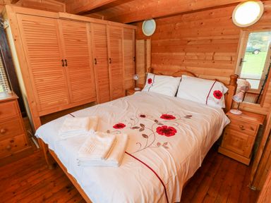 A bedroom with a double bed floral bedding wooden wardrobes bedside tables and folded towels at The Lodge in Rosemarket