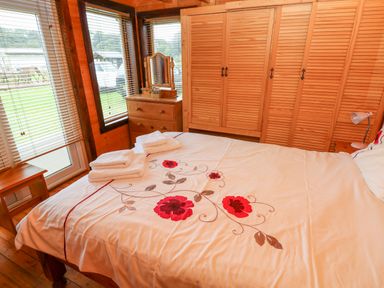 A bedroom with a bed with floral bedding folded towels wooden wardrobe and chest of drawers at The Lodge in Rosemarket