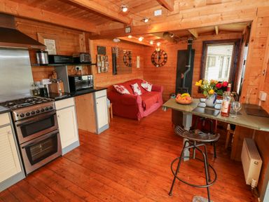 A wooden kitchen and living area with a red sofa a stove a small dining table with fruit and flowers at The Lodge in Rosemarket