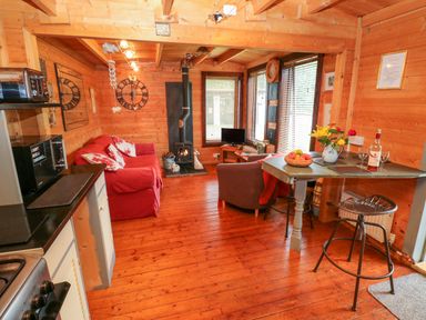A cabin living area with red sofa a wood stove a small dining table and kitchen appliances at The Lodge in Rosemarket