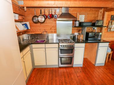 A kitchen with white cabinets a gas stove a microwave toaster and hanging pans at The Lodge in Rosemarket