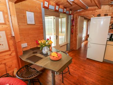 A kitchen corner with a table holding a vase of flowers and a fruit basket next to metal chairs and a white refrigerator at The Lodge Rosemarket