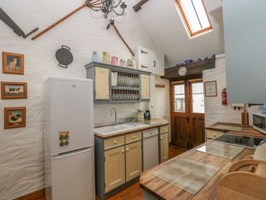 A kitchen with wooden countertops cupboards a refrigerator a sink and wooden double doors at Heather Cottage in Rosemarket