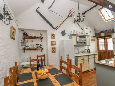 A kitchen with wooden dining table and chairs with black placemats and fruit bowl at Heather Cottage in Rosemarket