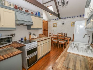 A kitchen with wooden countertops stove dining table wooden chairs and white sink at Heather Cottage in Rosemarket