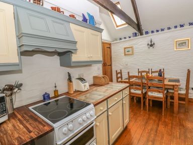 A kitchen with wooden floor cabinets stove dining table and chairs at Heather Cottage in Rosemarket