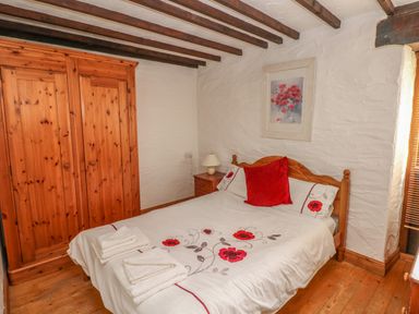 A bedroom with a wooden bed and wardrobe and floral bedding at Heather Cottage in Rosemarket