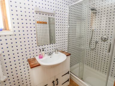 A bathroom with a sink and mirror next to a glass shower enclosure with tiled walls at Heather Cottage in Rosemarket