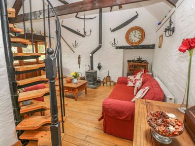 A living room with a red sofa wooden spiral staircase and a wood burning stove at Heather Cottage in Rosemarket