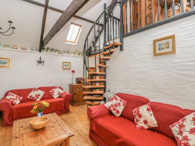 A living room with two red sofas and a wooden spiral staircase at Heather Cottage in Rosemarket