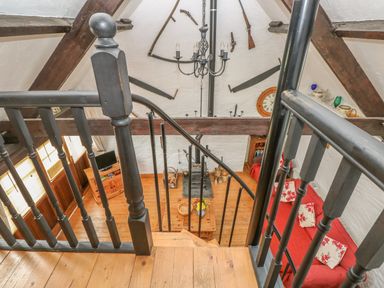 View of a living room with wooden floor a red sofa and a wood stove from a staircase with black railing at Heather Cottage in Rosemarket