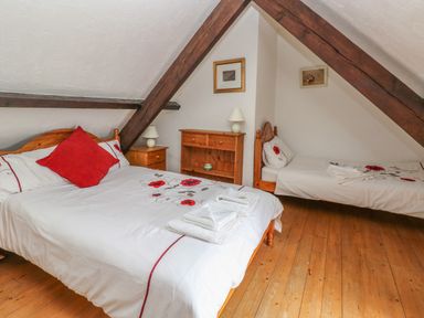 A bedroom with two beds wooden furniture and exposed wooden beams at Heather Cottage in Rosemarket