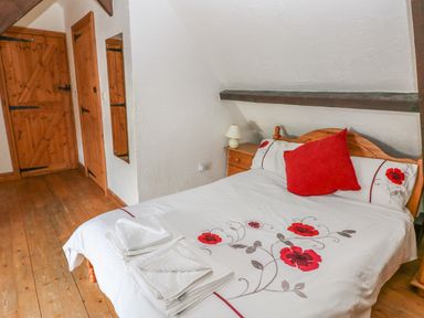 A bedroom with a wooden bed with floral bedding a bedside table with a lamp wooden doors and wooden floor at Heather Cottage in Rosemarket