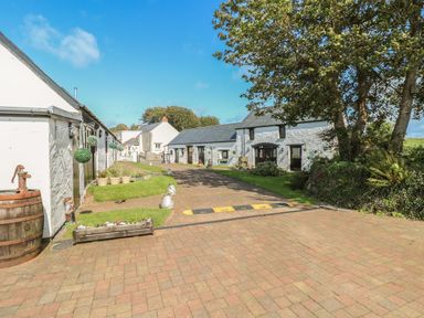 A paved driveway with white buildings on each side and trees on the right at Heather Cottage Rosemarket
