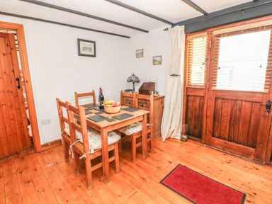 A dining area with wooden table and chairs next to wooden doors at Cowslip Cottage in Rosemarket