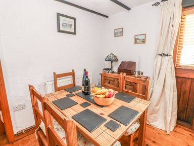 A dining room with a wooden table and chairs with placemats and a fruit bowl at Cowslip Cottage in Rosemarket