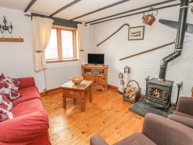 A living room with a red sofa a wood burning stove and wooden furniture at Cowslip Cottage in Rosemarket