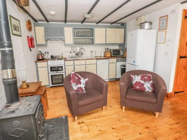 A kitchen with stove dishwasher and refrigerator and two armchairs with floral cushions at Cowslip Cottage in Rosemarket