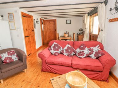 A living room with a red sofa and floral cushions a wooden dining table and chairs a brown armchair and wooden doors at Cowslip Cottage in Rosemarket