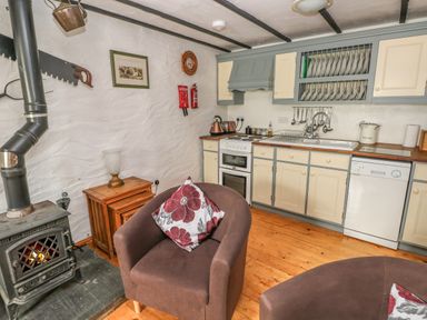 A kitchen with stove sink and dishwasher two armchairs with floral cushions and a wood burning stove at Cowslip Cottage Rosemarket