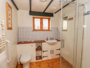 A bathroom with a toilet sink shower and wooden floor at Cowslip Cottage Rosemarket